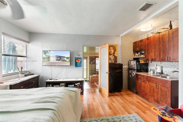 bedroom featuring light hardwood / wood-style floors, sink, black refrigerator, and ceiling fan