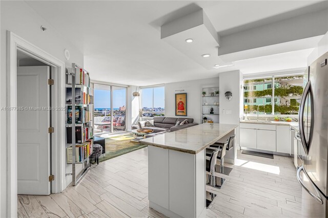 kitchen featuring light stone counters, recessed lighting, freestanding refrigerator, white cabinetry, and a kitchen island