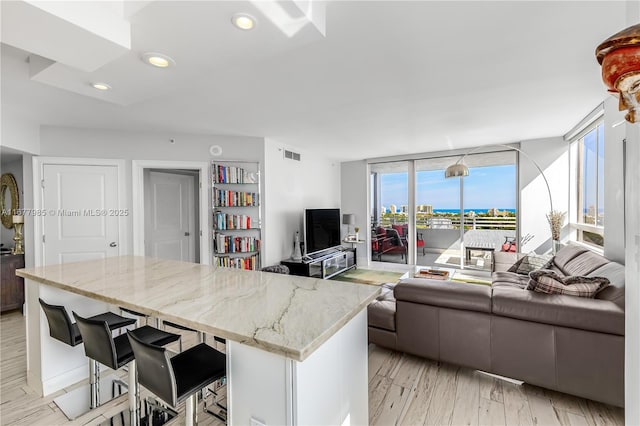 kitchen featuring a breakfast bar area, light hardwood / wood-style flooring, a wall of windows, light stone countertops, and white cabinets