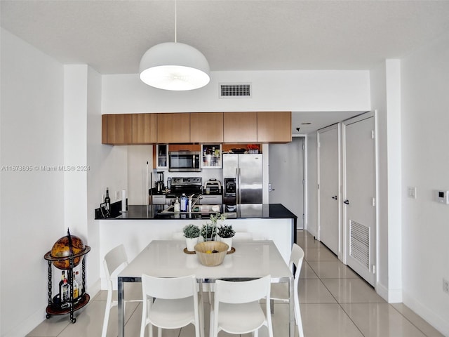 kitchen featuring kitchen peninsula, hanging light fixtures, stainless steel appliances, a kitchen bar, and light tile patterned floors