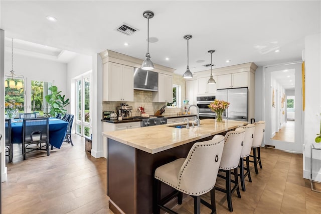 kitchen with wall chimney range hood, appliances with stainless steel finishes, sink, hardwood / wood-style floors, and hanging light fixtures