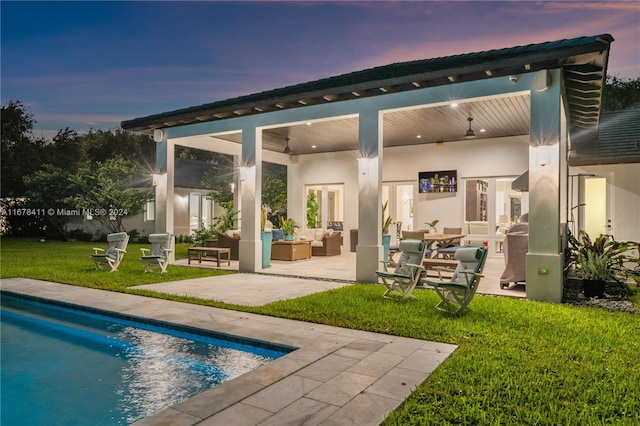 back house at dusk with an outdoor hangout area, a patio area, and a lawn