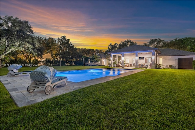 pool at dusk featuring a patio area and a lawn