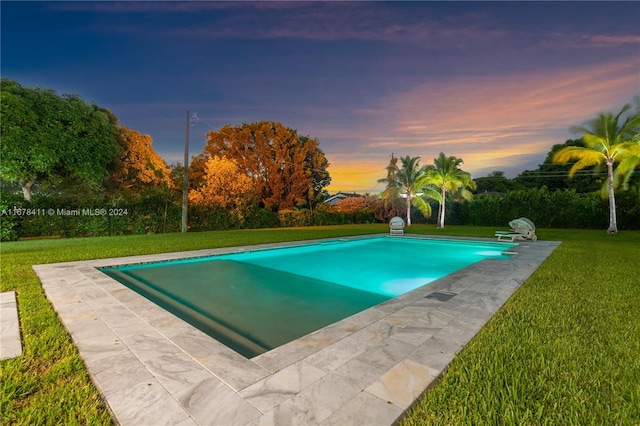 pool at dusk featuring a lawn