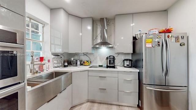 kitchen featuring wall chimney range hood, appliances with stainless steel finishes, white cabinets, decorative backsplash, and light hardwood / wood-style flooring