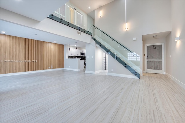 unfurnished living room featuring light wood-type flooring, a towering ceiling, and wooden walls