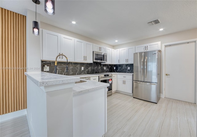 kitchen featuring kitchen peninsula, tasteful backsplash, hanging light fixtures, appliances with stainless steel finishes, and white cabinetry