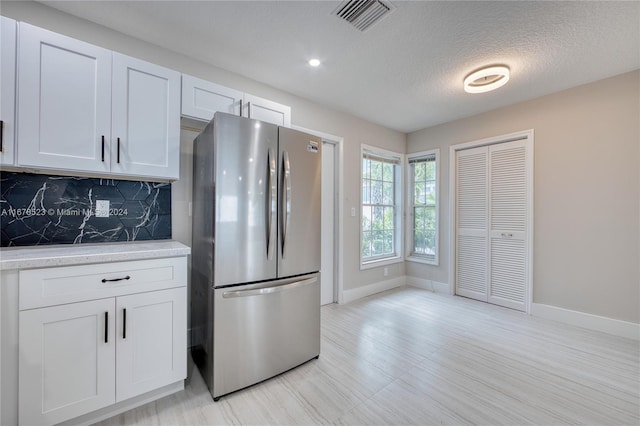 kitchen with stainless steel fridge, white cabinets, a textured ceiling, and tasteful backsplash