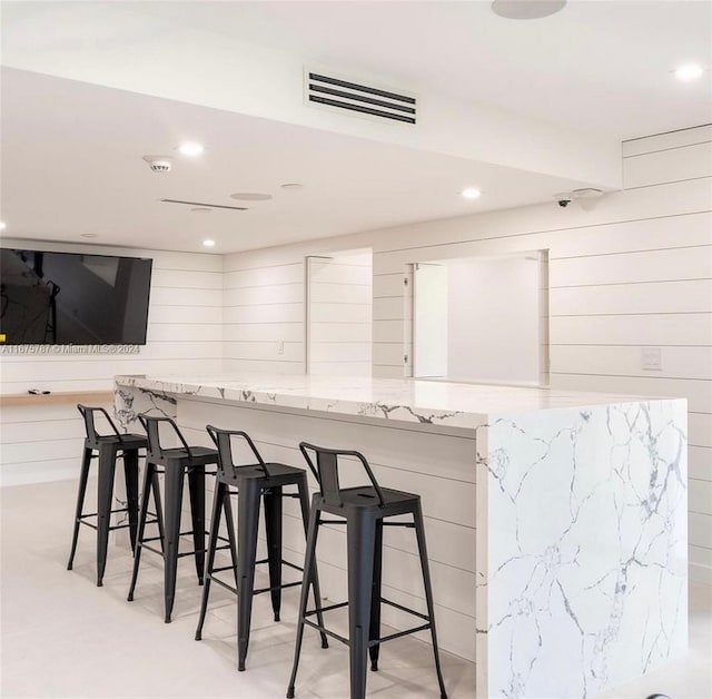 bar featuring white cabinetry, light stone counters, and wooden walls