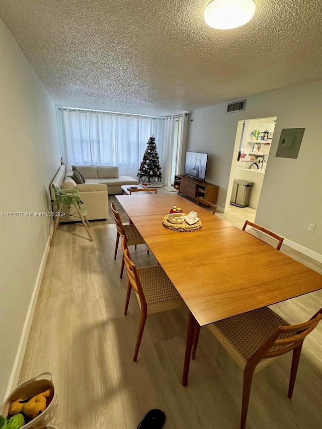 dining room featuring electric panel, light hardwood / wood-style floors, and a textured ceiling