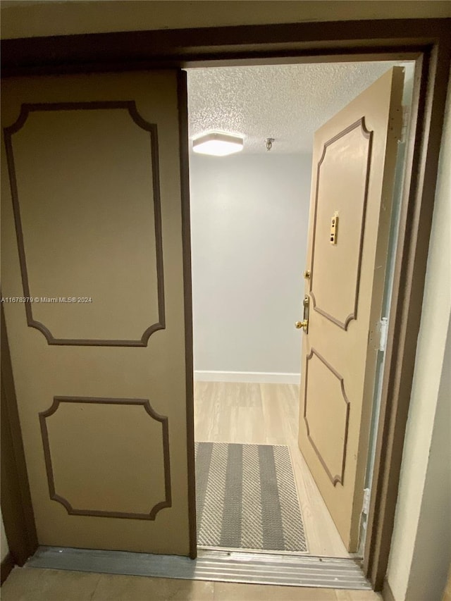 hall featuring light wood-type flooring and a textured ceiling