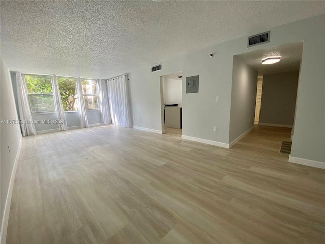 unfurnished living room with a textured ceiling, electric panel, and light hardwood / wood-style flooring