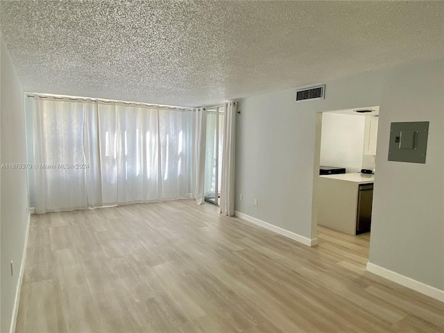 empty room with electric panel, a textured ceiling, and light wood-type flooring