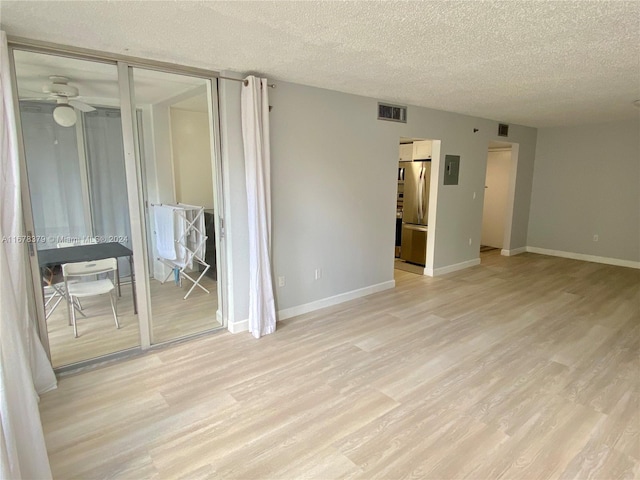 spare room featuring a textured ceiling, electric panel, and light hardwood / wood-style flooring