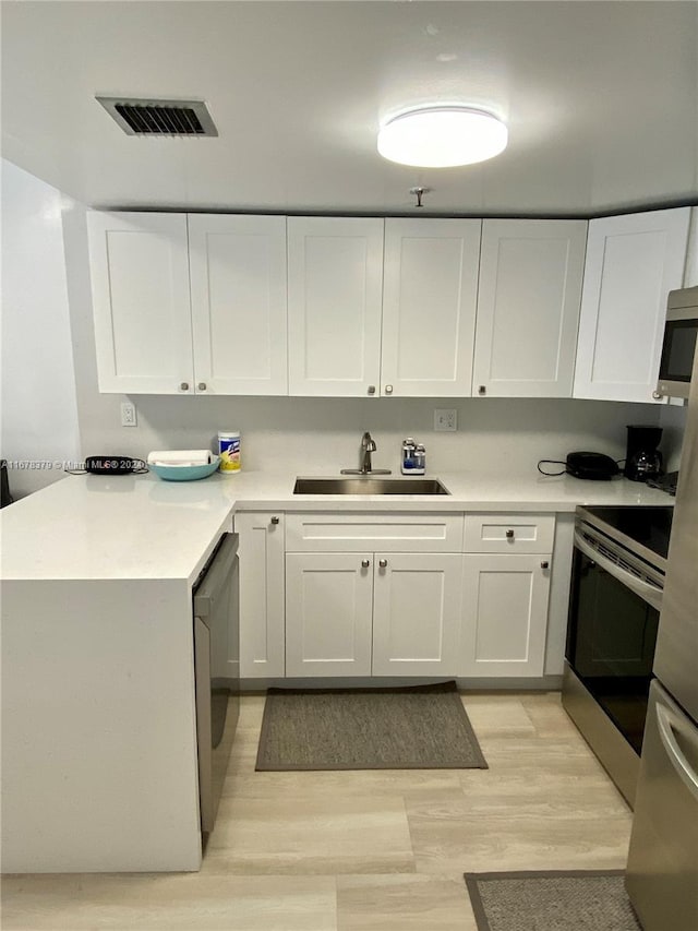 kitchen featuring sink, white cabinets, light hardwood / wood-style floors, and appliances with stainless steel finishes