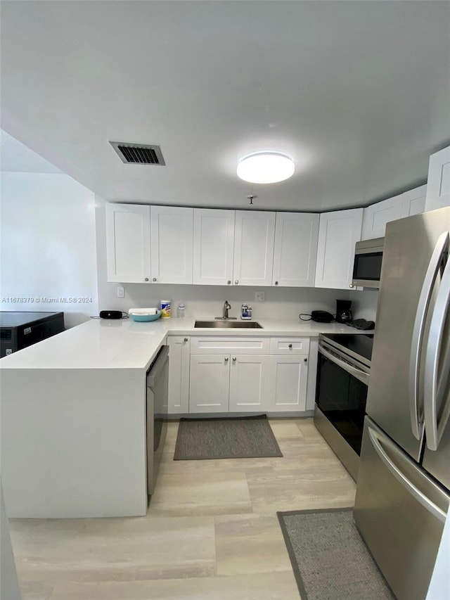 kitchen with white cabinets, appliances with stainless steel finishes, light hardwood / wood-style flooring, and sink