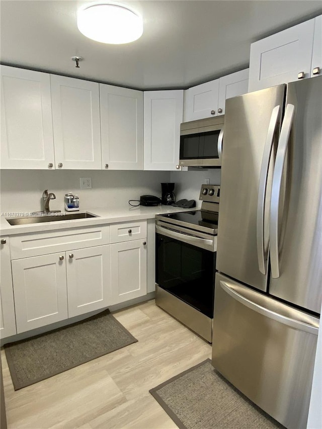 kitchen featuring white cabinets, sink, light wood-type flooring, and stainless steel appliances