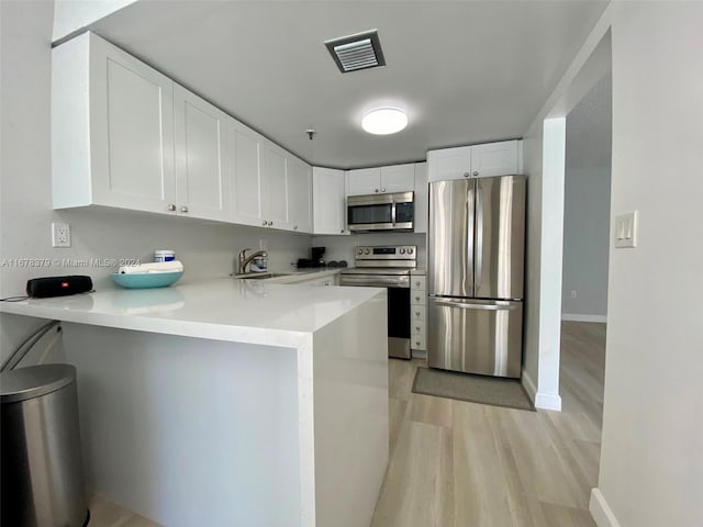 kitchen featuring white cabinetry, stainless steel appliances, a kitchen breakfast bar, light hardwood / wood-style flooring, and kitchen peninsula