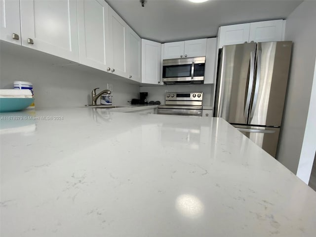 kitchen with white cabinets, light stone counters, sink, and stainless steel appliances