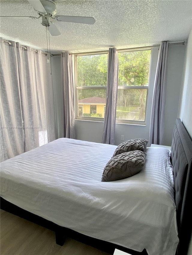 bedroom with ceiling fan, wood-type flooring, and a textured ceiling