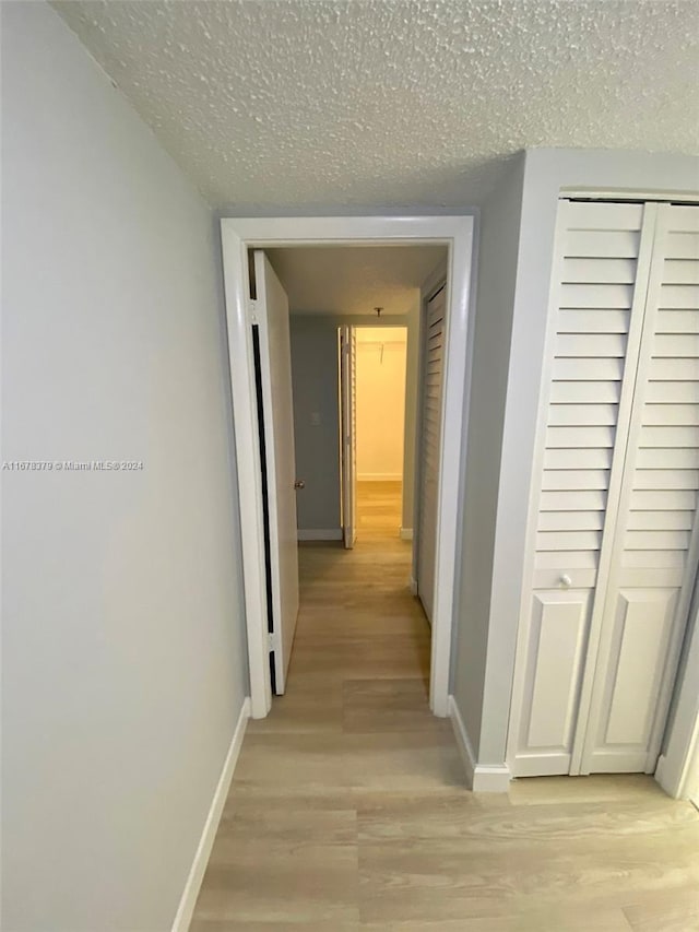 hall with light hardwood / wood-style floors and a textured ceiling