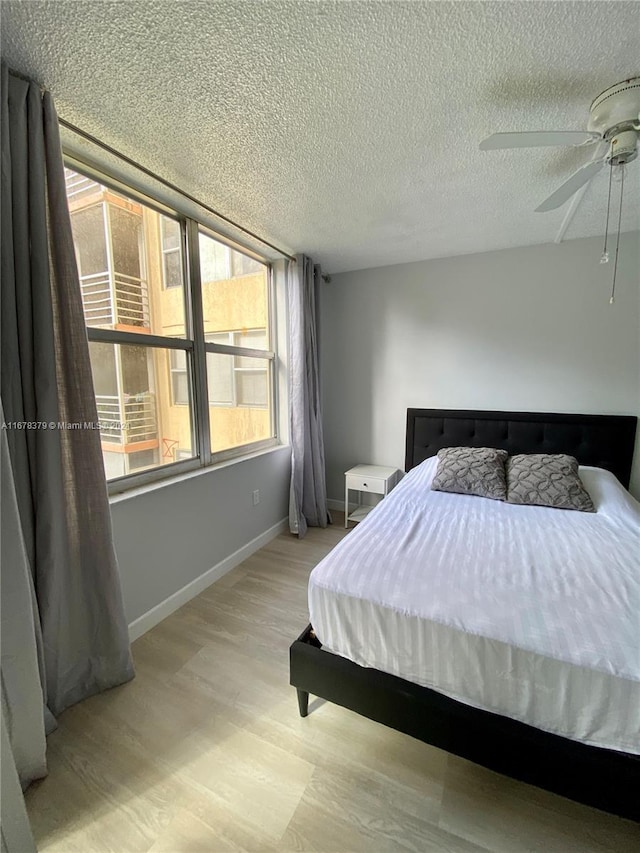 bedroom featuring ceiling fan, light hardwood / wood-style floors, and a textured ceiling