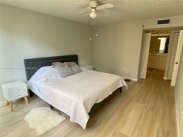 bedroom with ensuite bath, ceiling fan, a textured ceiling, and light wood-type flooring