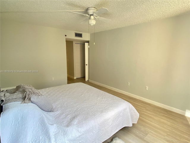 bedroom with a textured ceiling, light wood-type flooring, and ceiling fan