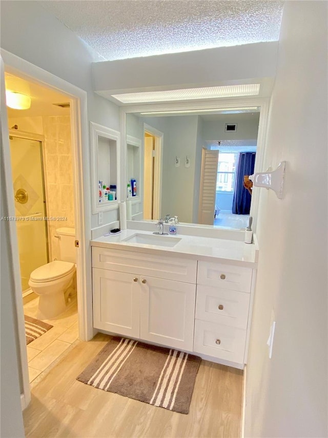 bathroom with vanity, a textured ceiling, a shower with door, hardwood / wood-style flooring, and toilet