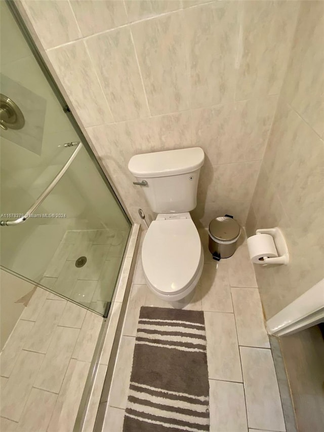 bathroom featuring tile patterned floors, a shower with door, tile walls, and toilet