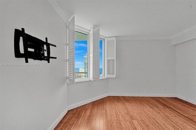 empty room with light hardwood / wood-style floors, ornamental molding, and a textured ceiling