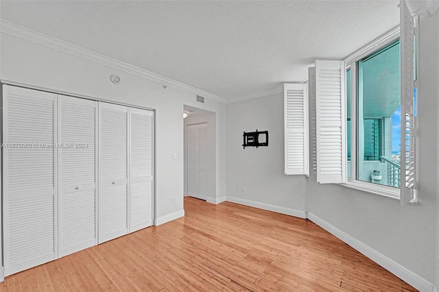 unfurnished bedroom with a closet, crown molding, a textured ceiling, and light wood-type flooring