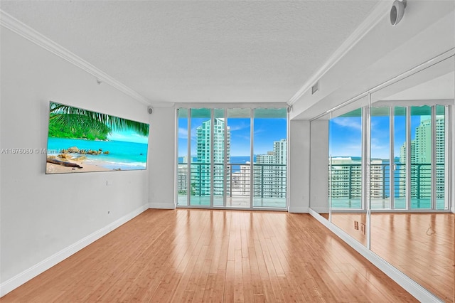 unfurnished room featuring a wealth of natural light, ornamental molding, expansive windows, and wood-type flooring