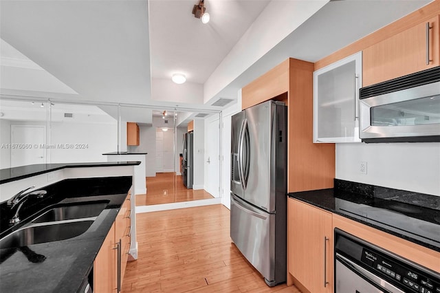 kitchen with light brown cabinetry, light hardwood / wood-style flooring, dark stone countertops, sink, and stainless steel appliances