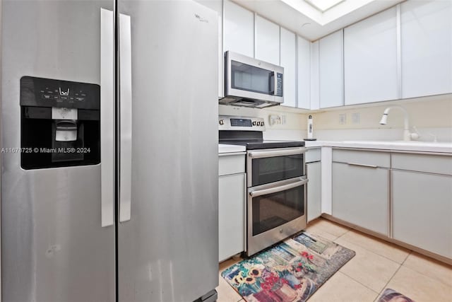 kitchen featuring appliances with stainless steel finishes, white cabinetry, light tile patterned flooring, and sink