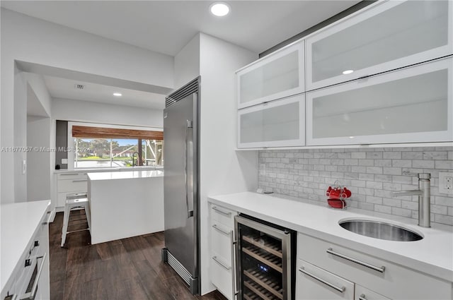 bar with sink, built in fridge, white cabinets, dark wood-type flooring, and wine cooler