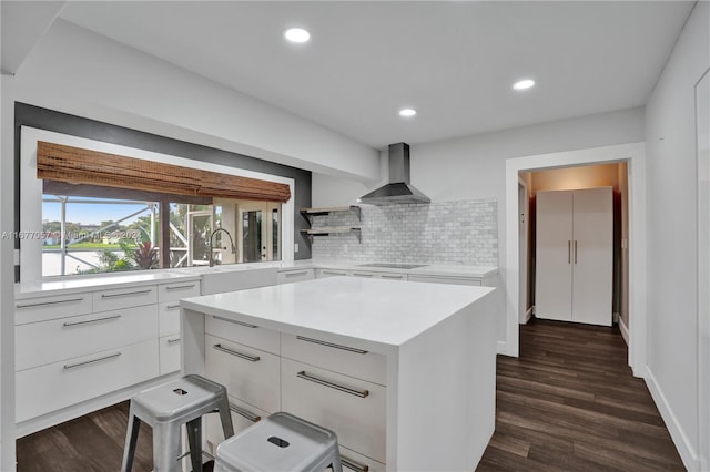 kitchen featuring decorative backsplash, a kitchen island, wall chimney exhaust hood, dark wood-type flooring, and white cabinets