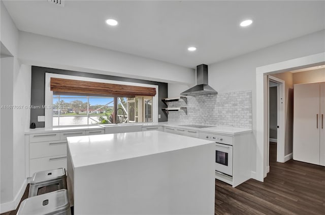 kitchen with a kitchen island, dark hardwood / wood-style floors, oven, wall chimney exhaust hood, and white cabinets