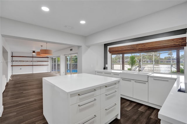 kitchen featuring a kitchen island, sink, decorative light fixtures, white cabinets, and dark hardwood / wood-style flooring