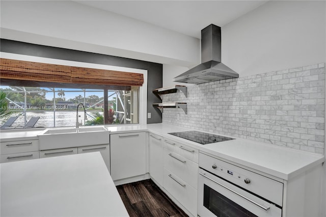 kitchen with open shelves, white oven, black electric stovetop, light countertops, and wall chimney exhaust hood