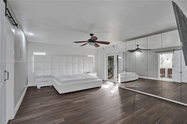 unfurnished bedroom with dark wood-type flooring, a barn door, and ceiling fan