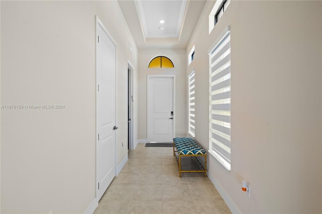 hallway with crown molding, a tray ceiling, a healthy amount of sunlight, and light tile patterned floors