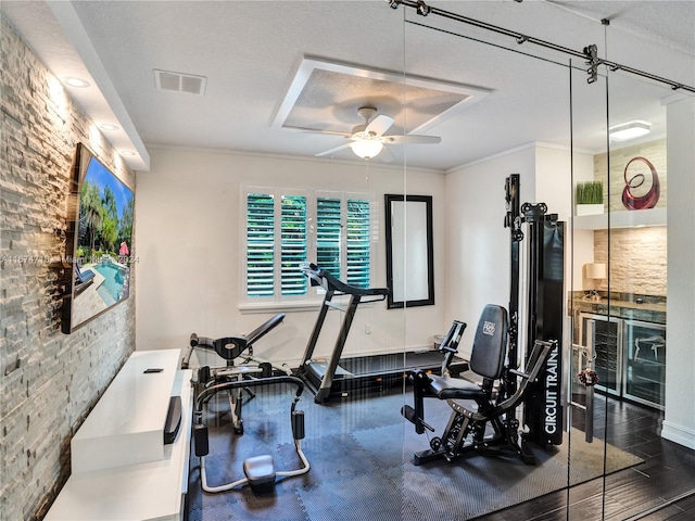 exercise room featuring ornamental molding, a textured ceiling, dark wood-type flooring, and ceiling fan