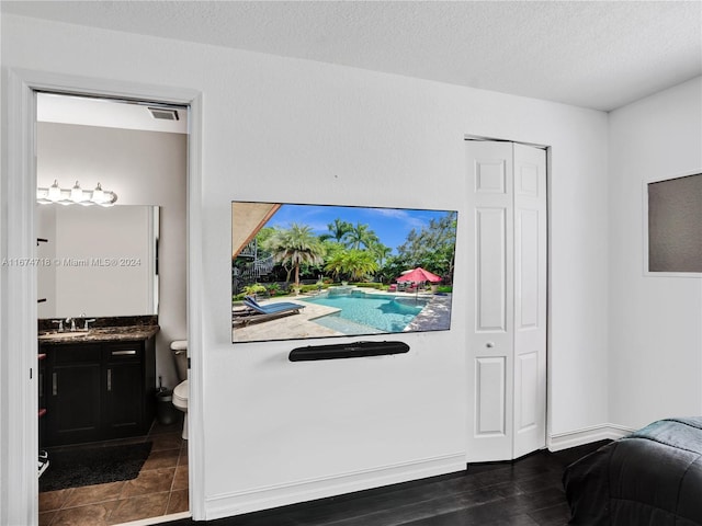 bedroom with connected bathroom, a closet, sink, a textured ceiling, and dark hardwood / wood-style flooring