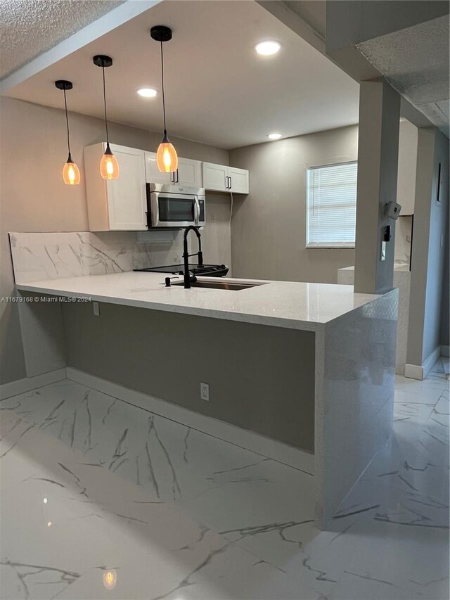 kitchen with white cabinets, marble finish floor, a sink, stainless steel microwave, and a peninsula