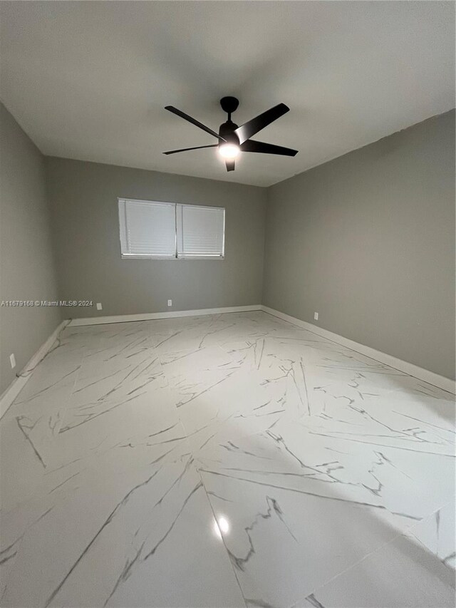 empty room with marble finish floor, a ceiling fan, and baseboards