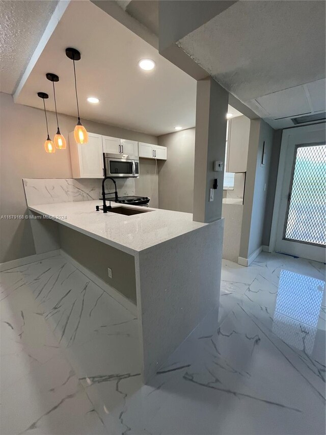 kitchen featuring a peninsula, stainless steel microwave, baseboards, white cabinetry, and marble finish floor