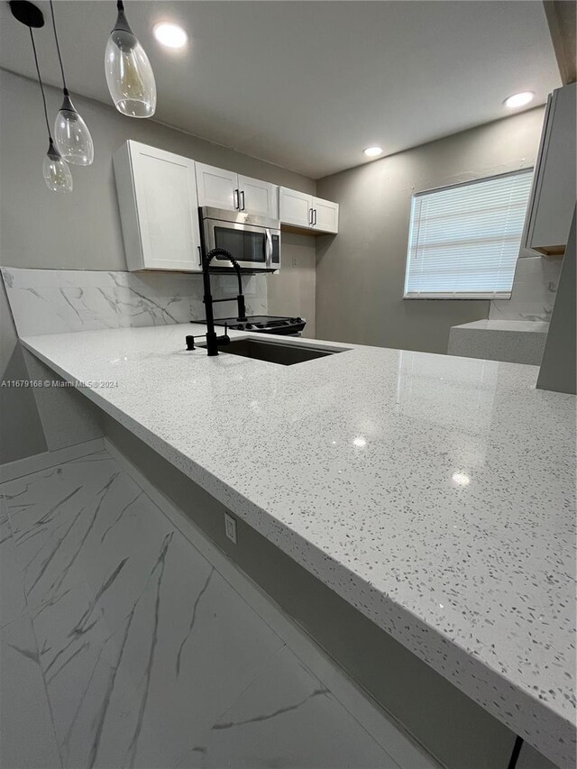 kitchen with white cabinets, a sink, stainless steel microwave, decorative light fixtures, and light stone countertops