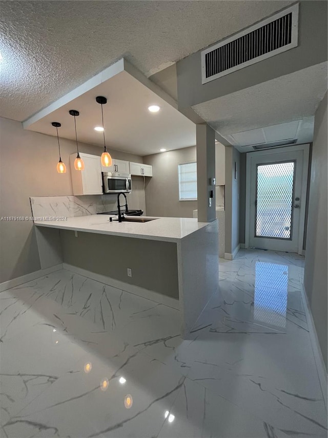 kitchen with kitchen peninsula, sink, pendant lighting, white cabinets, and a textured ceiling