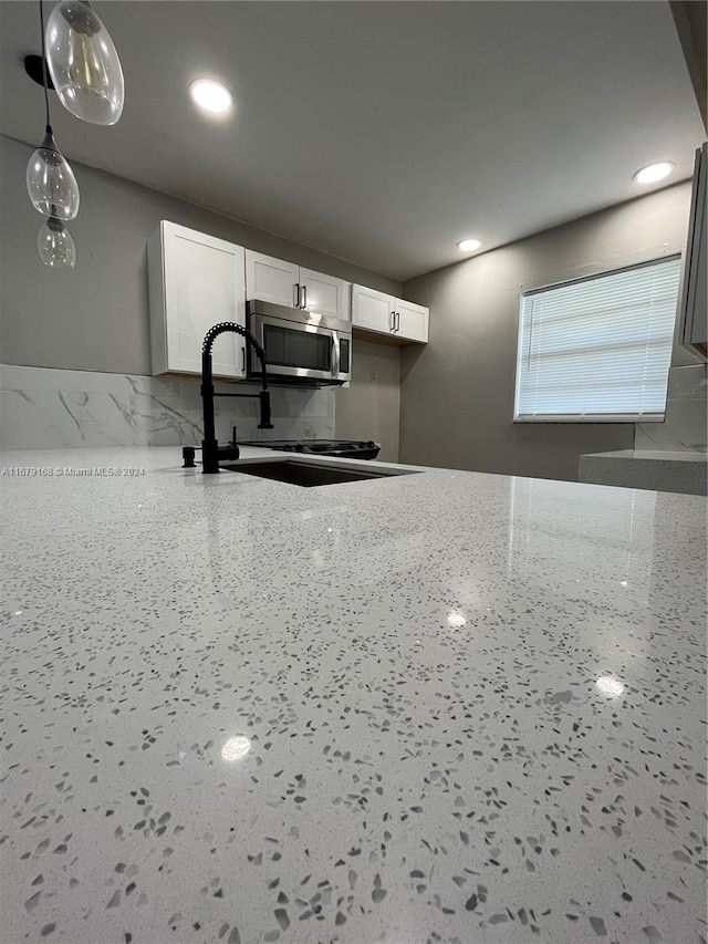 kitchen featuring sink, light stone counters, decorative light fixtures, and white cabinets